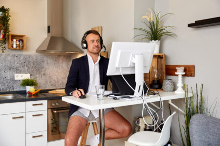 A man is taking part in an online video conference wearing a shirt and jacket but no trousers